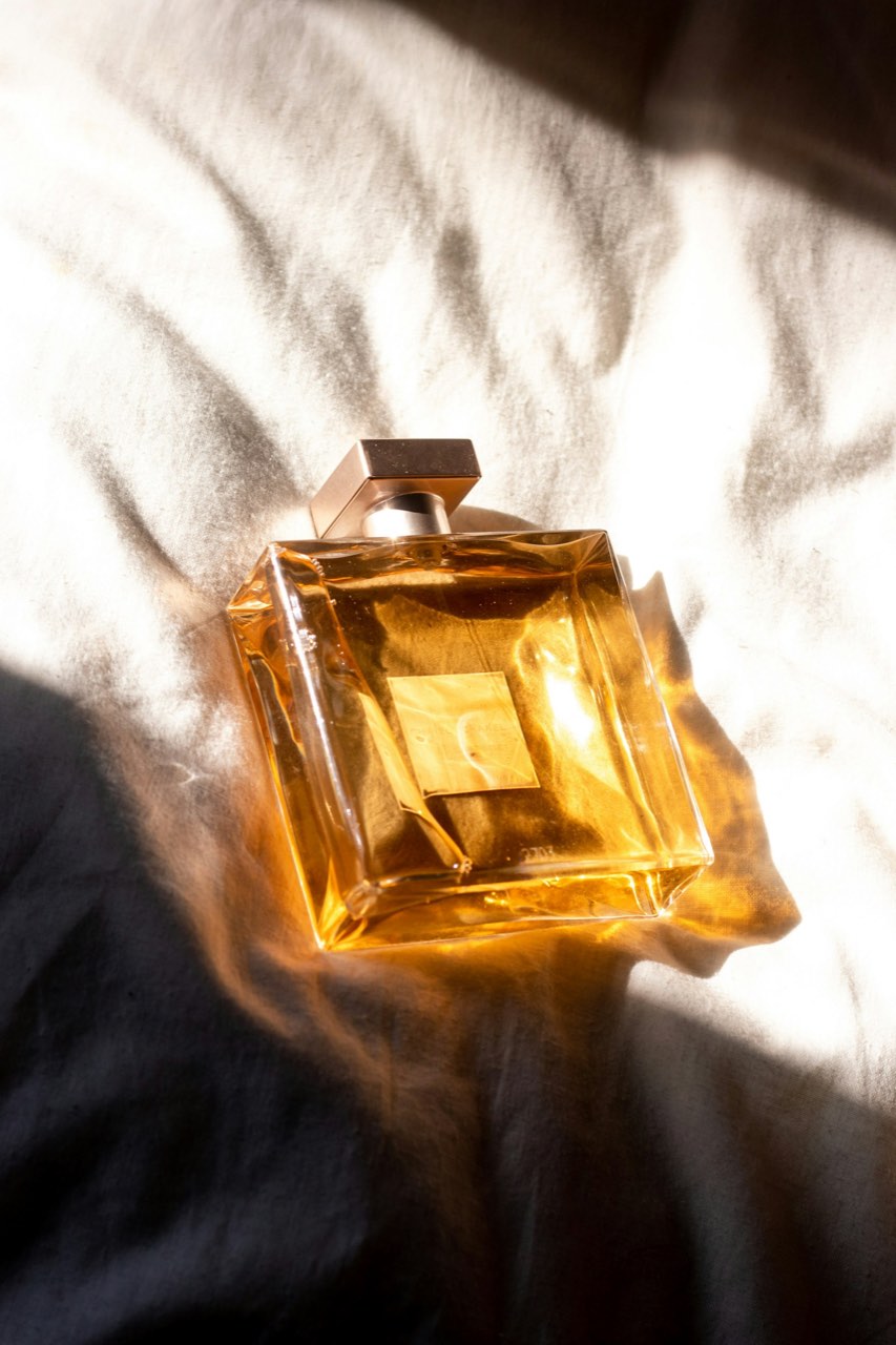 Golden perfume bottle resting on draped fabric in warm sunlight